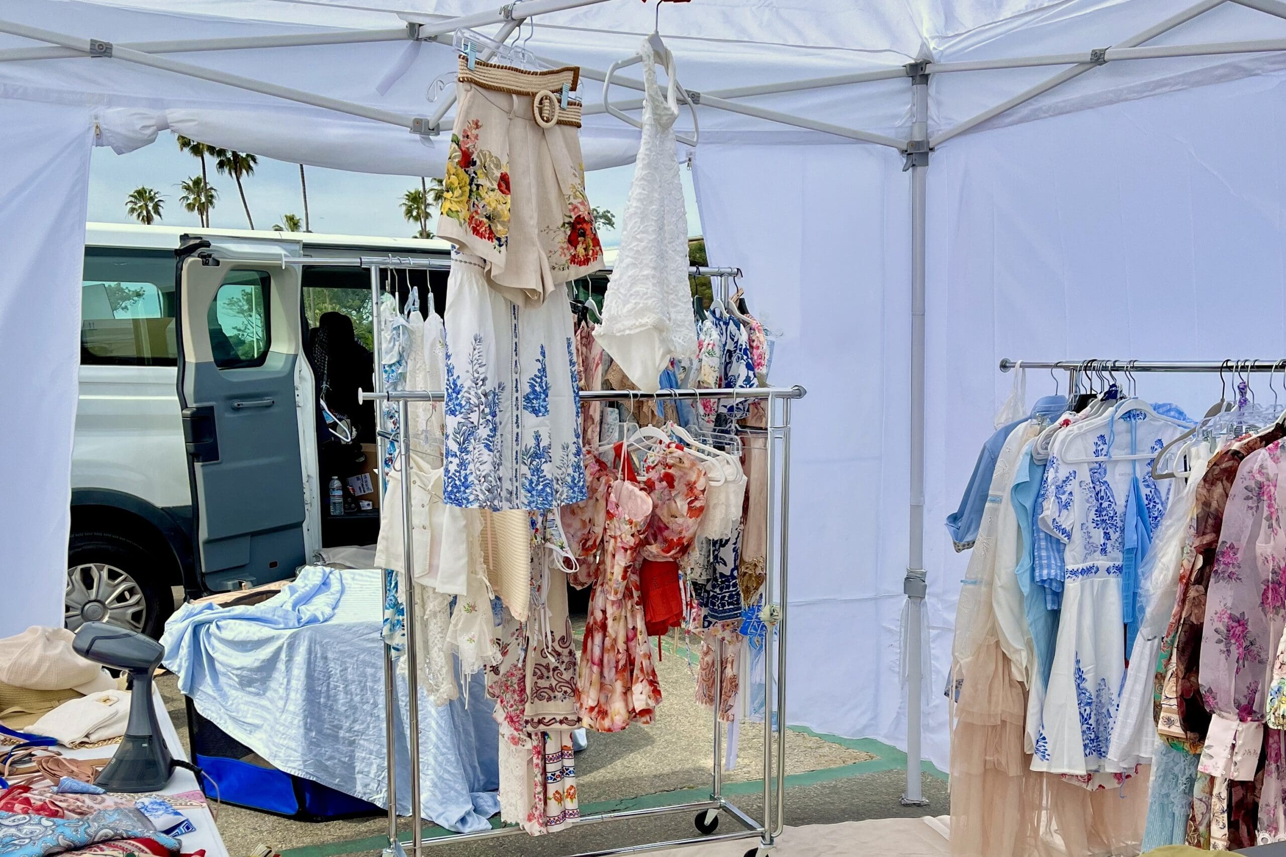 Clothing racks crowded with floral dresses, skirts, and tops under a white canopy tent, illustrating too many wardrobe options before a headshot session